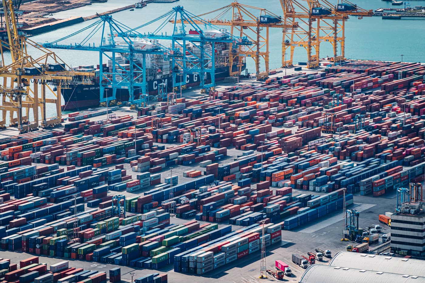 Aerial view of a container terminal: gantry cranes over a container ship and rows of containers on the quay.