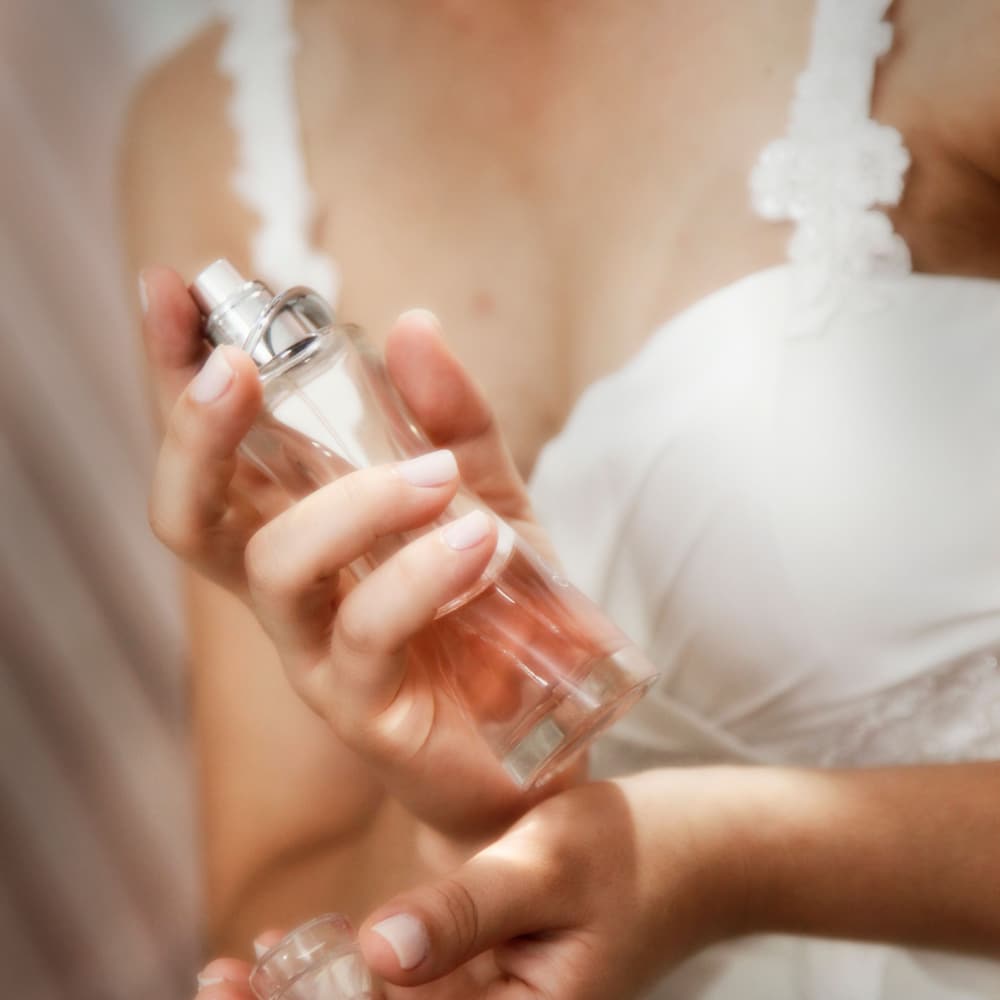A woman holding a glass perfume bottle, about to spray it on her wrist.