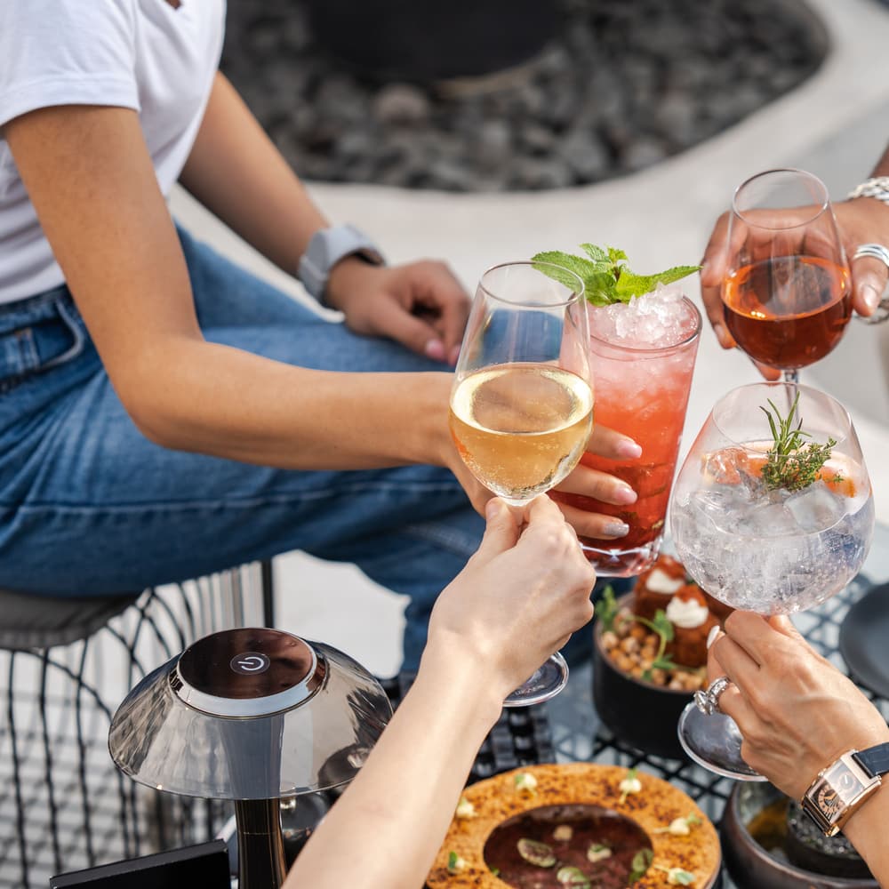 Four people raising cocktails and sparkling wine over a table set with food.