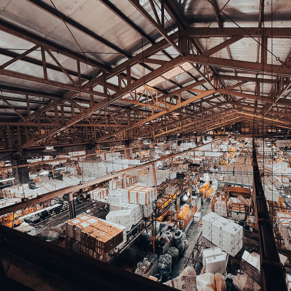 A wholesale warehouse from above: goods packed and sorted across the floor under a steel roof.